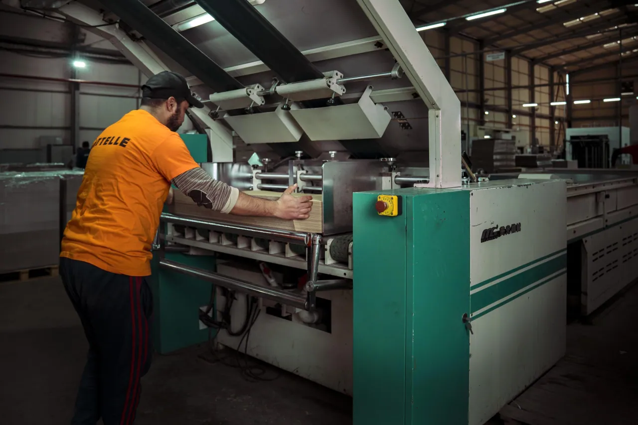 Opérateur en t-shirt orange SITTELLE introduisant une pile de carton dans l'entrée d'une grande machine verte et blanche.