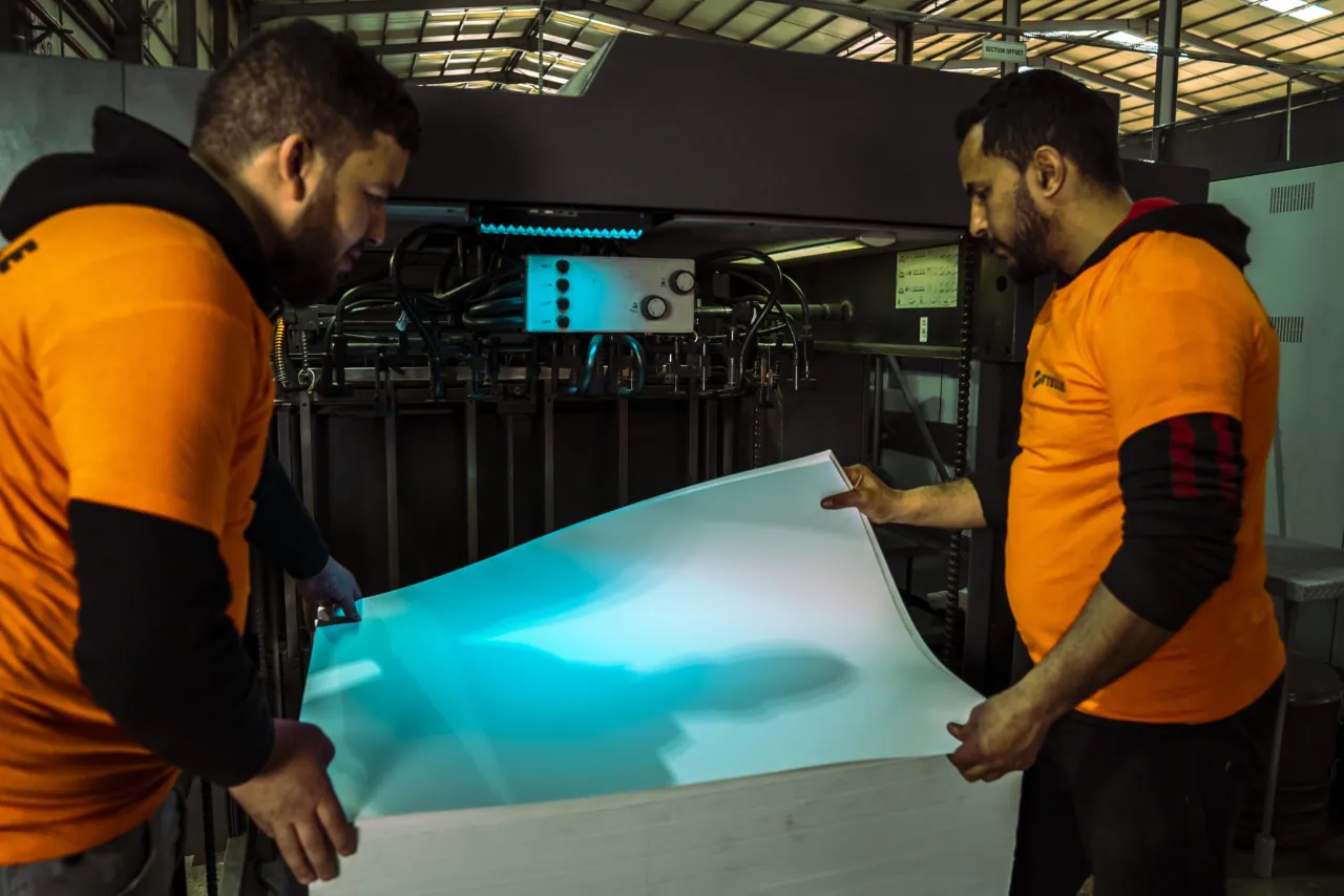 Deux opérateurs en t-shirts orange SITTELLE tenant une grande feuille blanche devant la presse offset, panneau « SECTION OFFSET ».